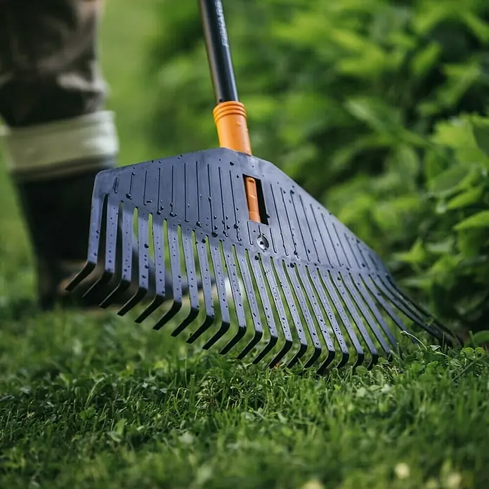 Fiskars Solid Laubbesen - Arbeitsbreite: 52 cm, Anzahl Zinken: 24, Art Stiel: Langstiel - Nahaufnahme eines schwarzen Fiskars-Laubrechens, der auf einem grünen Rasen liegt, ideal für Gartenarbeiten und die Entfernung von Laub.