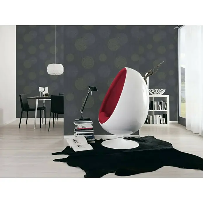 A.S. Création Casual Living Vliestapete Kreise - Anthrazit-Grau, Grafisch, 10,05 x 0,53 m - Ein Ei-förmiger Sessel mit roter Innenseite steht auf einem schwarzen Teppich. Bücher und eine Lampe stehen neben dem modernen Sessel.