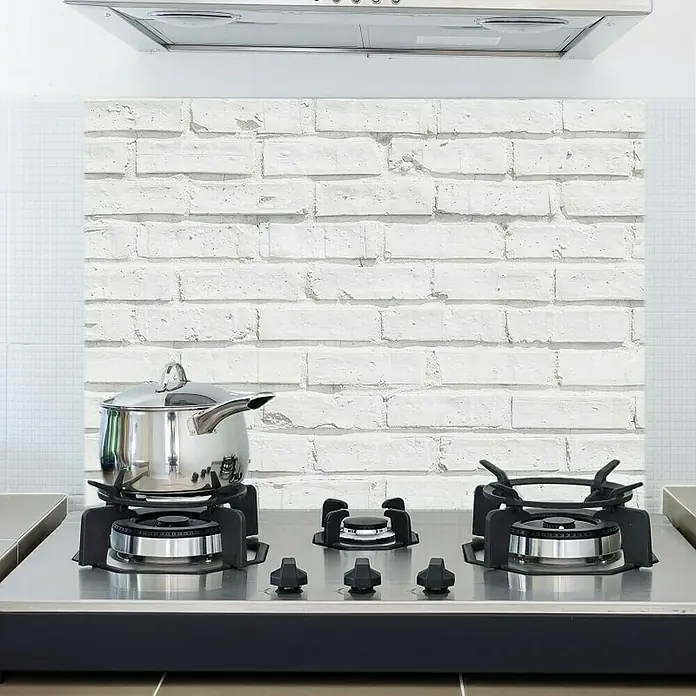 Protector de pared de cocina adhesivo Ladrillo - 47 x 67 cm - Encimera empotrada con placa de acero inoxidable y tres quemadores bajo una campana extractora, complementada con una olla de acero inox.