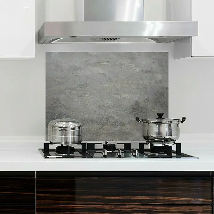 Protector de pared de cocina adhesivo Concreto - 65 x 47 cm - Placas de cocción de vidrio con ollas de acero inoxidable en una encimera de cocina blanca frente a un protector contra salpicaduras gris.