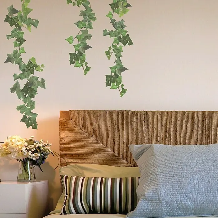 Vinilo de pared Hiedra Verde - Verde, Plástico - Vista detallada de un dormitorio con cabecero de mimbre, cojines decorativos, una mesita de noche con flores y enredaderas de hiedra colgantes.