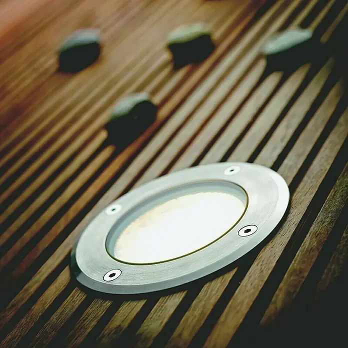 Starlux Bodeneinbauleuchte Arvika - 5 W, Warmweiß - Nahaufnahme einer eingelassenen Terrassenleuchte aus Metall, die auf einem Holzdeckboden für stimmungsvolle Beleuchtung sorgt.
