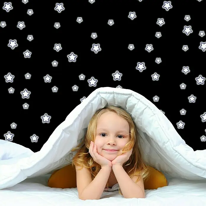 Vinilo de pared Stars - 15,5 x 34 cm, Blanco con borde azul, Plástico - Niña sonriente bajo una manta blanca en una cama con fondo de cielo estrellado, representando una escena acogedora e imaginativa.