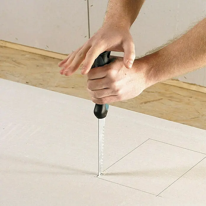 Wolfcraft Gipskartonplatten-Stichsäge - Geeignet für: Gipskartonplatten - Nahaufnahme eines Mannes, der eine Gipskartonplatte mit einer Stichsäge bearbeitet, um eine saubere, rechteckige Aussparung zu erstellen.