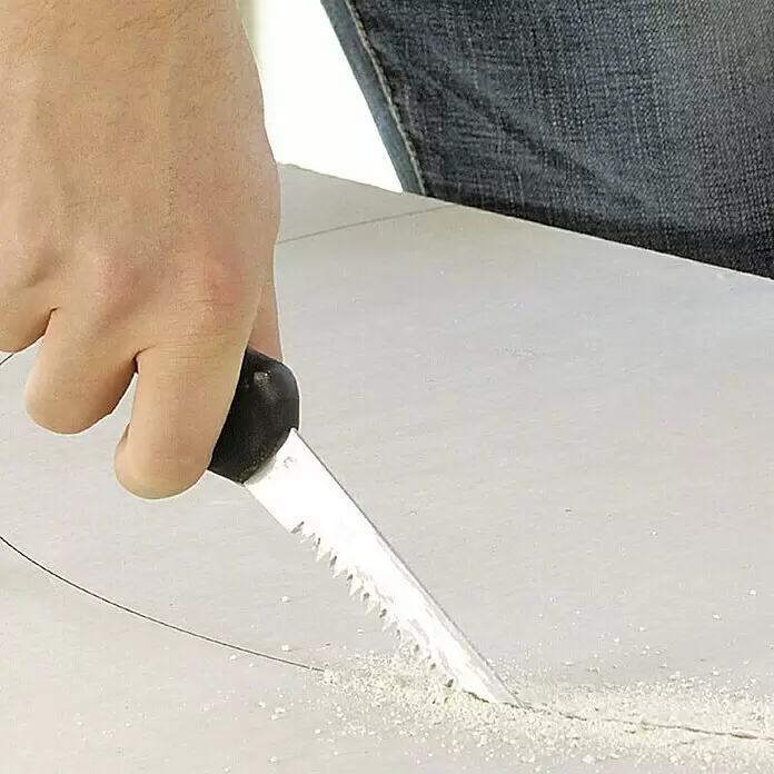 Wolfcraft Gipskartonplatten-Stichsäge - Geeignet für: Gipskartonplatten - Hand hält Stichsäge mit gezackter Metallklinge und schwarzem Griff, sägt in helle Platte, erzeugt Staub.