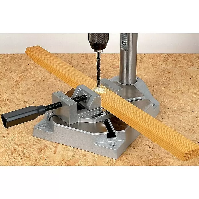 Wolfcraft Soporte de taladro - L x An x Al: 307 x 203 x 570 mm, Apertura máxima: 60 mm - Soporte de taladro plateado con mordaza sujetando una tabla de madera para perforar. Una broca perfora un agujero, creando serrín.