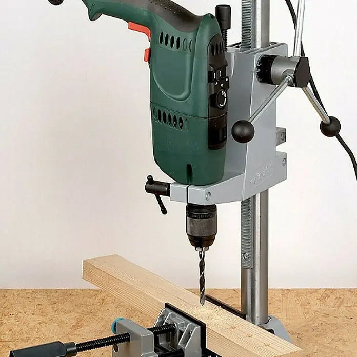 Wolfcraft Soporte de taladro - L x An x Al: 307 x 203 x 570 mm, Apertura máxima: 60 mm - Un taladro de banco está perforando un agujero en un trozo de madera, que está sujeto con una abrazadera.