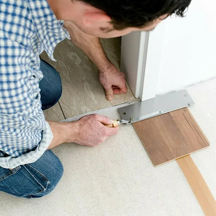 Wolfcraft Sierra de mano 6925000 - Largo: 39 cm - Primer plano de una persona cortando un marco de puerta con una sierra de corte al ras para instalar un suelo de madera perfectamente ajustado.
