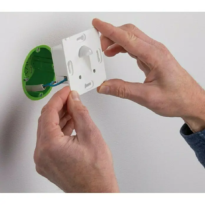 Paulmann LED-Einbauleuchte eckig - 2,7 W, Weiß, L x B: 7,8 x 7,8 cm, Eckig - Nahaufnahme einer Person, die einen Bewegungsmelder an einer Wand mit grüner Installationsdose befestigt.