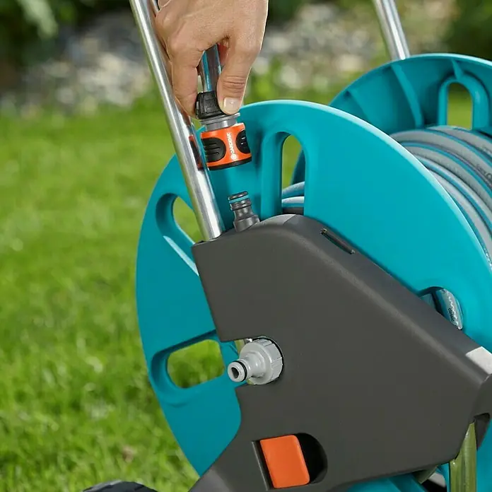 Gardena Carro portamangueras CleverRoll M Easy - Plástico/metal, Capacidad de manguera: 60 m, 13 mm (½'') - Primer plano de una persona que conecta una manguera de jardín a un portamangueras GARDENA.