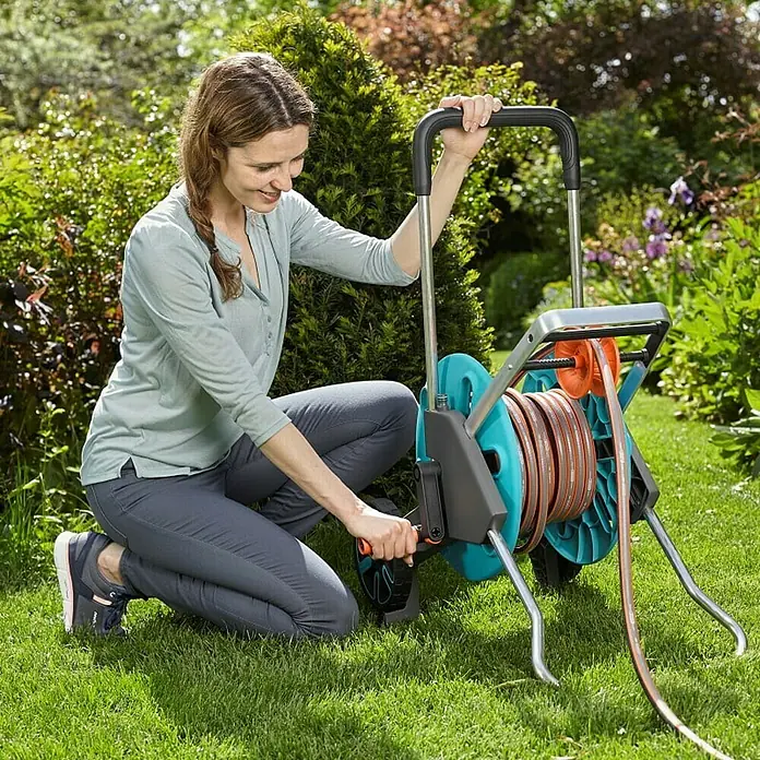 Gardena Carro portamangueras CleverRoll M Easy - Plástico/metal, Capacidad de manguera: 60 m, 13 mm (½'') - Mujer girando una caja de manguera Gardena RollUp M/L para enrollar una manguera de jardín.