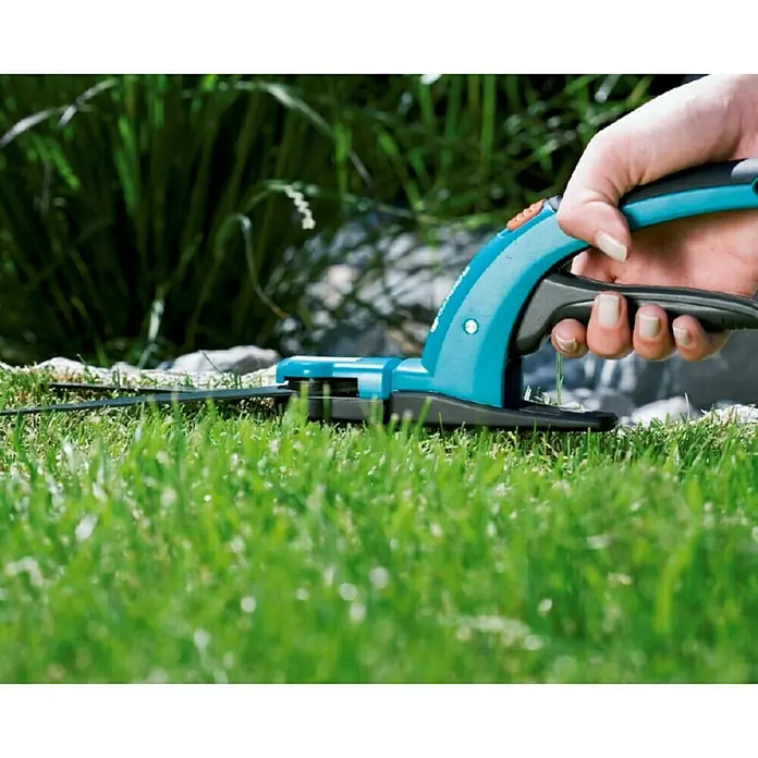 Gardena Comfort Grasschere - Material Klinge: Geschliffene Schneide, Antihaftbeschichtet - Nahaufnahme einer Hand, die eine Gardena Akku-Grasschere in einem Garten benutzt, um Rasen zu schneiden.