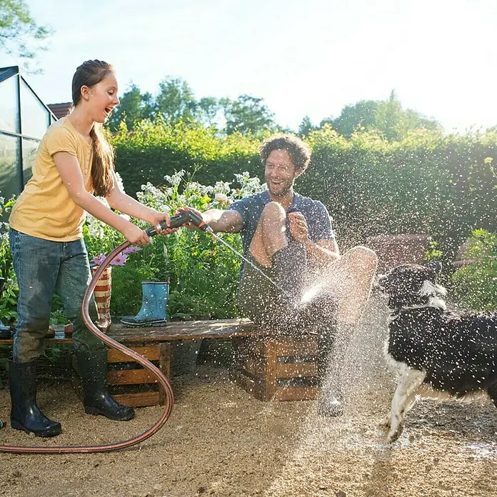 Gardena Premium Reinigungsspritze - Anzahl Sprühformen: 3 Stk., Metall/Kunststoff - Ein Mädchen gießt mit einem Gardena-Gartenschlauch einen Mann und einen Hund im Garten, die eine lustige und erfrischende Zeit haben.