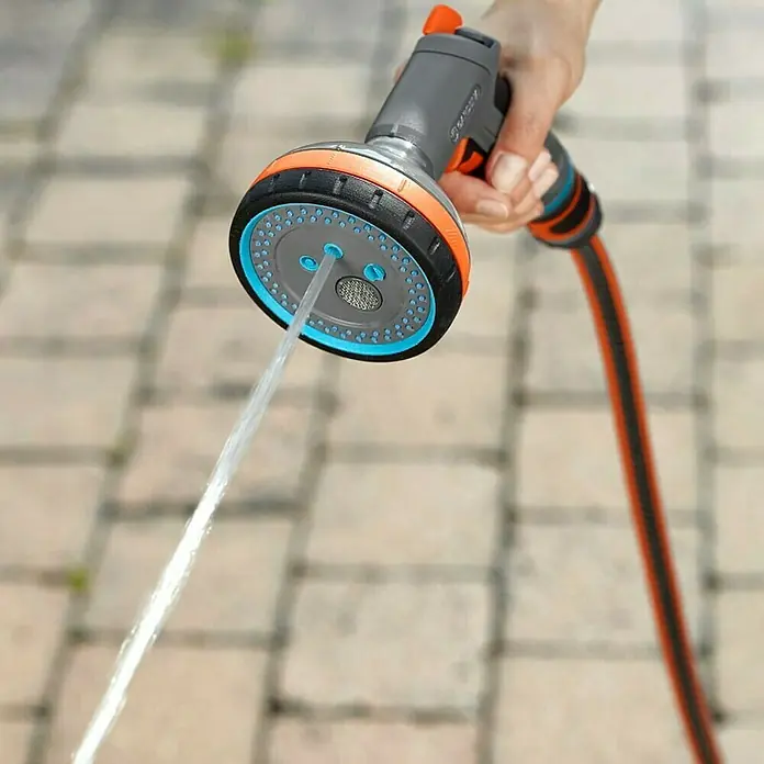 Gardena Comfort Multibrause - Anzahl Sprühformen: 5 Stk., Metall/Kunststoff - Nahaufnahme eines Mehrzweck-Gartenbrausekopfs von Gardena in Betrieb, der Wasser auf eine gepflasterte Fläche sprüht.