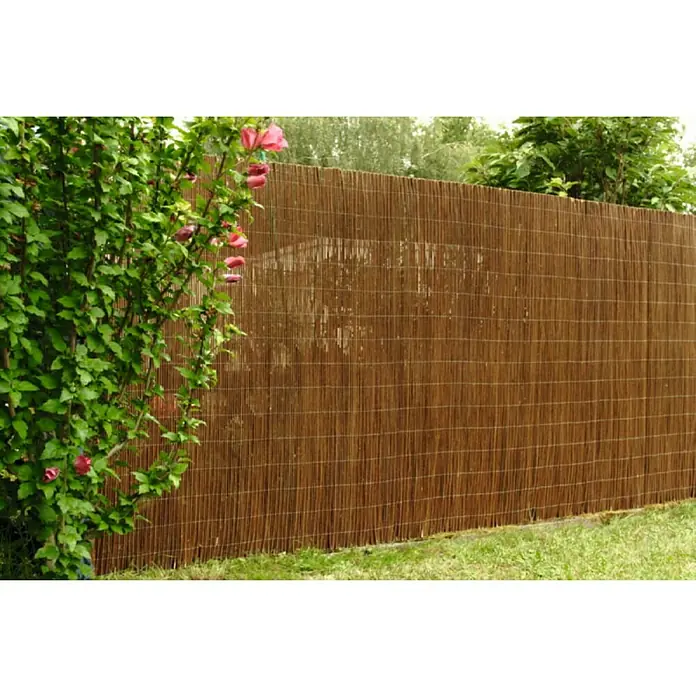 Gardol Weidenmatte Classic - Weide, 300 x 90 cm - Ein brauner, geflochtener Bambuszaun im Garten, der Privatsphäre bietet und von einem blühenden Busch geschmückt wird.