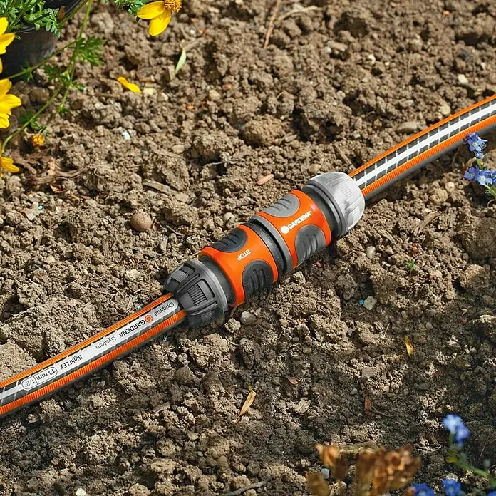 Gardena Schlauchkupplung - ½″ - Nahaufnahme eines Gardena Schlauchstücks auf Gartenerde, das zwei Enden eines Gartenschlauchs verbindet.