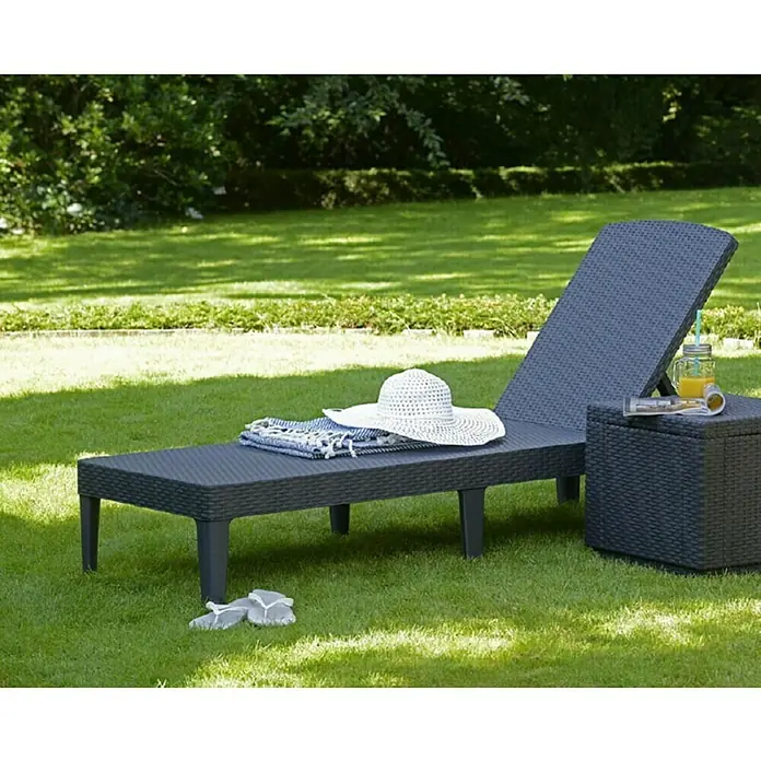 Allibert Sonnenliege Jaipur - B x T x H: 58 x 187 x 29 cm, Graphit, 4-fach verstellbare Rückenlehne - Sonnenliege mit Beistelltisch im Garten. Die Liege ist aus dunklem Rattan gefertigt und mit einem Handtuch und einem Hut dekoriert.
