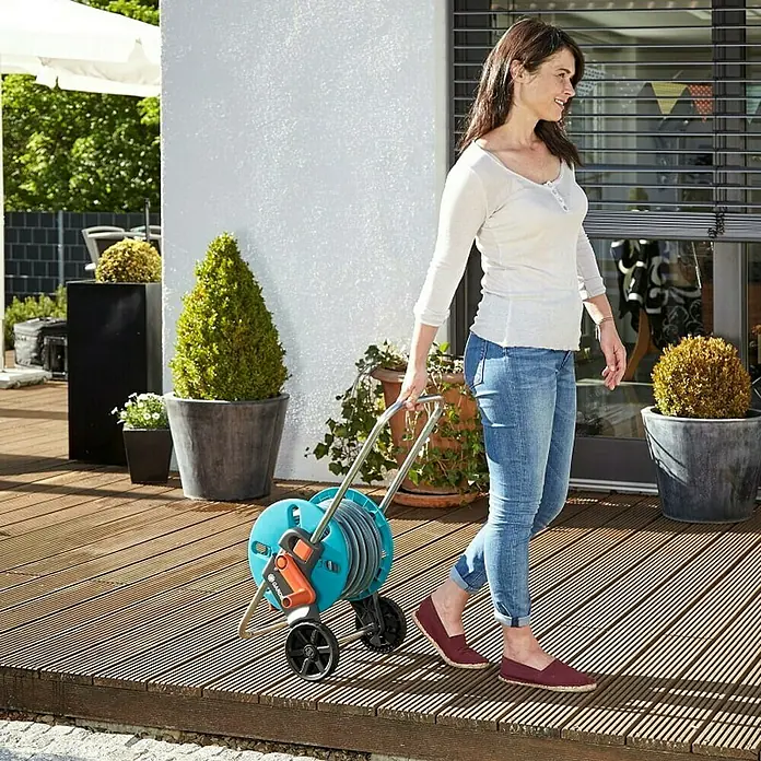 Gardena Schlauchwagen-Set CleverRoll S - Kunststoff/Metall, Schlauchlänge: 20 m - Frau zieht einen GARDENA Schlauchwagen auf einer Holzterrasse. Praktische und mühelose Gartenbewässerung mit dem GARDENA Schlauchwagen.