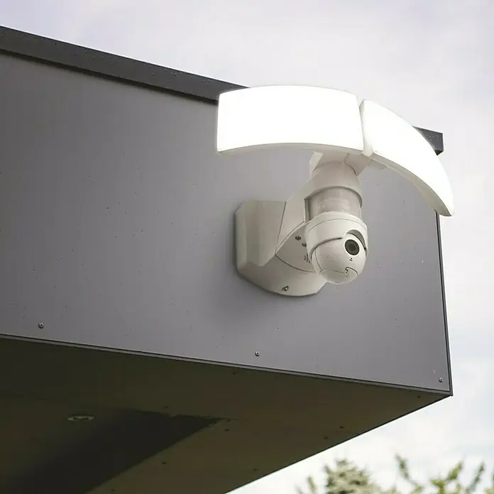Lutec Proyector LED Libra doble con sensor y cámara - 38 W, L x An x Al: 227 x 309 x 202 mm, Blanco, Blanco frío - Una moderna cámara de seguridad blanca con dos luces LED está montada en una pared gris, proporcionando vigilancia e iluminación.