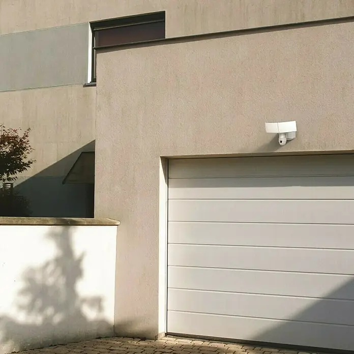 Lutec Proyector LED Libra doble con sensor y cámara - 38 W, L x An x Al: 227 x 309 x 202 mm, Blanco, Blanco frío - Exterior de una casa con un garaje blanco y una cámara de seguridad blanca con focos instalada.