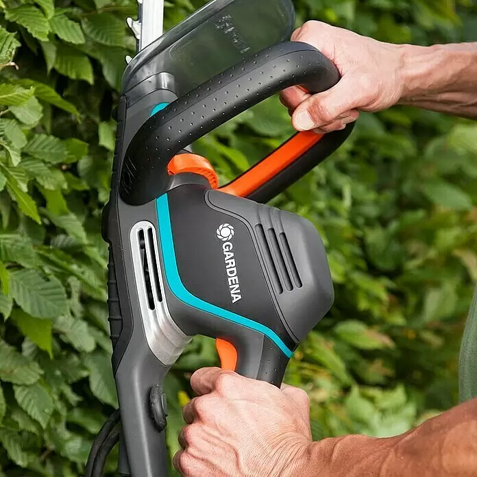 Gardena PowerCut Cortasetos eléctrico 700/65 - 700 W, Longitud de corte: 65 cm - Un cortasetos Gardena negro y gris con detalles turquesas es sujetado por dos manos, podando setos.