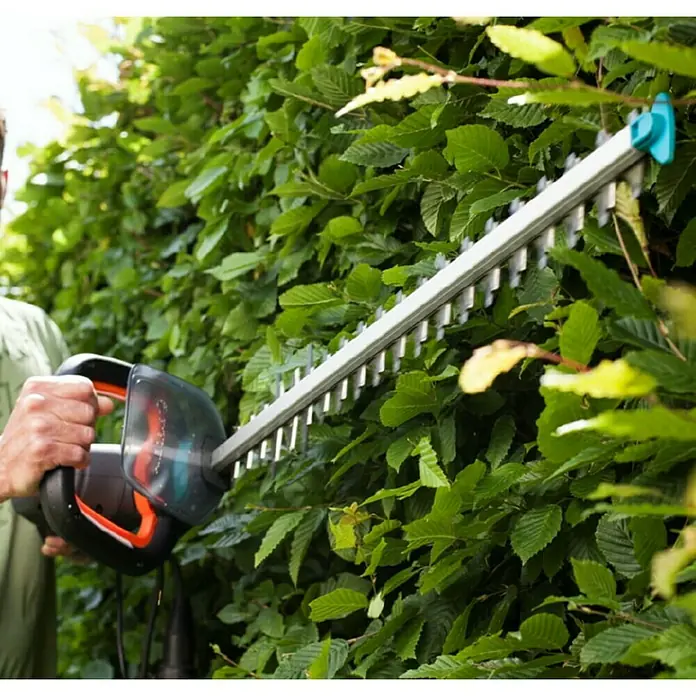 Gardena PowerCut Cortasetos eléctrico 700/65 - 700 W, Longitud de corte: 65 cm - Un cortasetos Gardena utilizado para recortar un exuberante seto verde en un jardín.