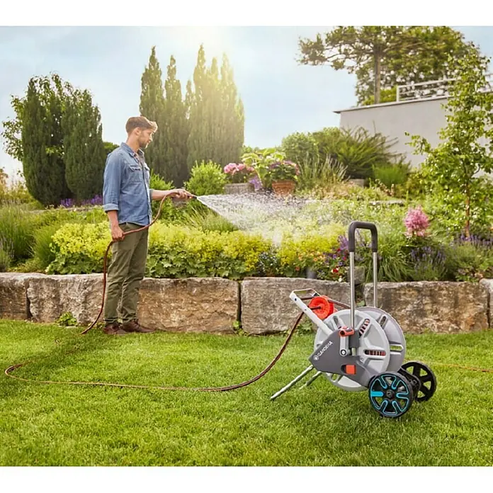 Gardena Schlauchwagen-Set CleverRoll M - Kunststoff/Metall, Schlauchlänge: 25 m - Ein Mann bewässert seinen Garten mit einer Gardena Schlauchbox. Die Schlauchbox ist grau mit blauen Akzenten.