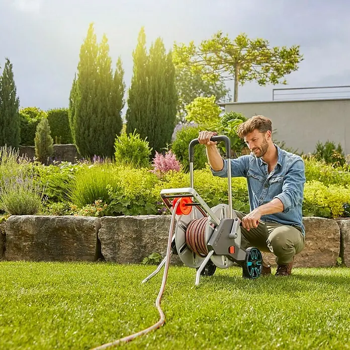 Gardena Schlauchwagen-Set CleverRoll M - Kunststoff/Metall, Schlauchlänge: 25 m - Ein Mann benutzt eine Gardena Schlauchtrommel im Garten. Die Trommel ist grau und orange, mit einem aufgerollten Schlauch.
