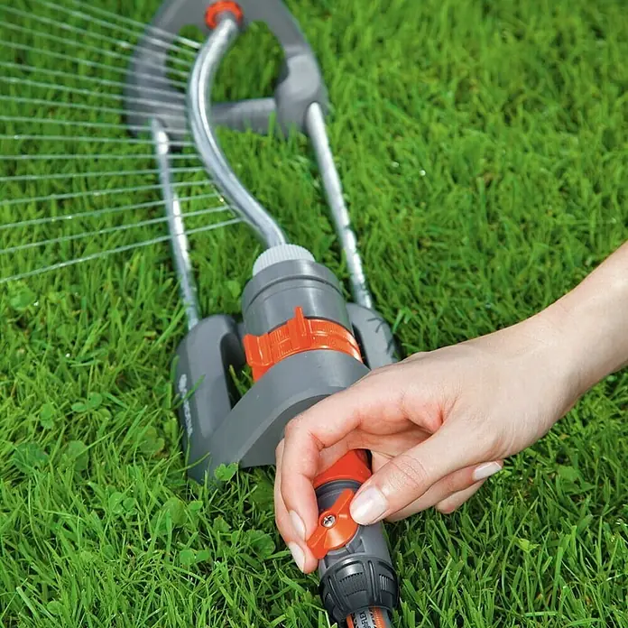Gardena Regulierstop - Größe: ½″ - Eine Person stellt den Wasserdurchfluss eines Gardena Regners mit einem roten Ventil ein, der auf einem grünen Rasen steht.