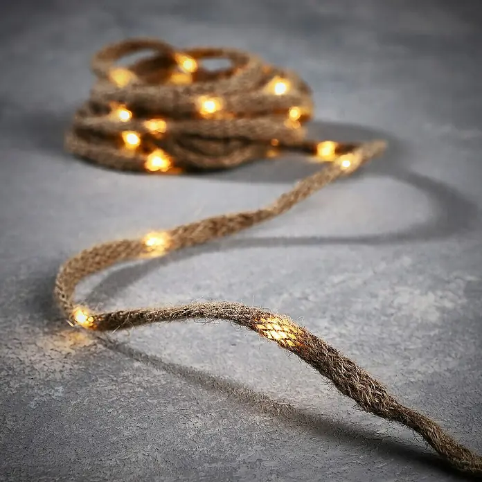 Tira de luces LED Cuerda -  - Cálidas luces de cuerda de yute enrolladas y extendidas sobre una superficie gris, creando un ambiente acogedor.