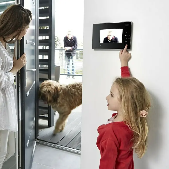 Legrand Monitor de interfono adicional 7" - Negro - Comunicación moderna de puerta: mujer abre la puerta, niña usa el intercomunicador. Foco en tecnología para el hogar.