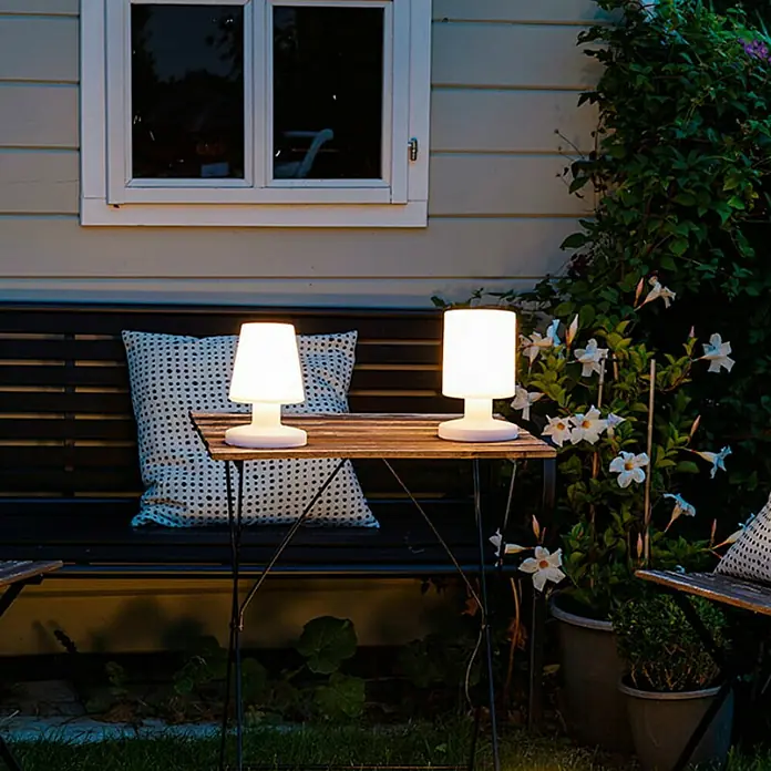 Reality Leuchten Akku-Tischleuchte Dora - 1,5 W, L x B x H: 13 x 13 x 21 cm, Weiß, Warmweiß - Zwei kabellose Tischleuchten mit warmem Licht auf einem Gartentisch. Die Lampen spenden eine gemütliche Atmosphäre für den Abend.