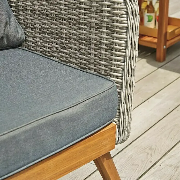 Sunfun Loungemöbel-Set Sina - 4 -tlg., Aluminium, Akazie, Polyrattan, Bambusgrau/Braun - Nahaufnahme eines grauen Rattansessels mit blauem Kissen und einem Holzgestell auf einer Holzterrasse mit einem Beistelltisch im Hintergrund.