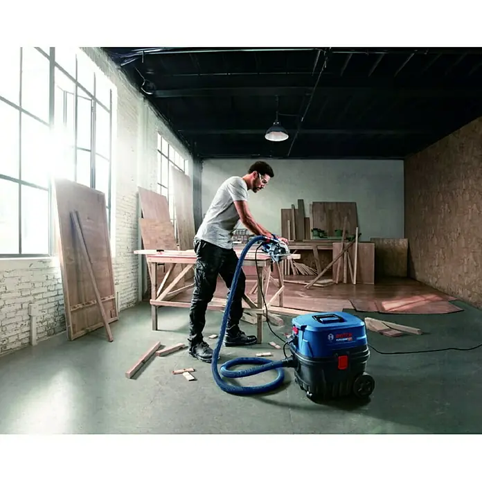 Bosch Professional Elektro-Nass- & Trockensauger GAS 12-25 PL - 1.250 W, Behältervolumen: 25 l, Mit Beutel - Ein Handwerker benutzt einen Bosch-Staubsauger, um Staub beim Holzsägen aufzusaugen. Der robuste Sauger sorgt für Sauberkeit in der Werkstatt.