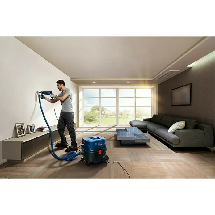 Bosch Professional Elektro-Nass- & Trockensauger GAS 12-25 PL - 1.250 W, Behältervolumen: 25 l, Mit Beutel - Ein Mann bohrt mit einem Bosch Bohrhammer ein Loch in eine Wand, an den ein Bosch-Staubsauger angeschlossen ist.