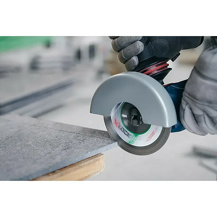 Bosch Professional X-Lock Disco de corte X-Lock Best for Ceramic - Ø x Es: 125 x 1 mm, Orificio: 22,23 mm - Imagen de una mano cortando baldosas con una amoladora. La amoladora angular con disco de corte corta el material con precisión.