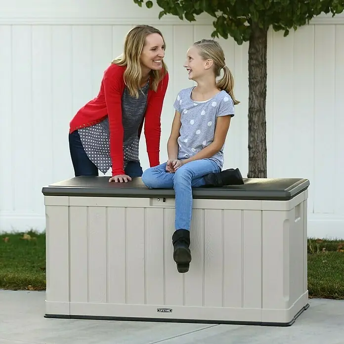 Lifetime Gartenbox Harmony - 128 x 64 x 67 cm, Lichtgrau, Kunststoff - Eine Mutter und ihre Tochter sitzen auf einer Lifetime Aufbewahrungsbox im Freien, die zusätzlichen Stauraum bietet.