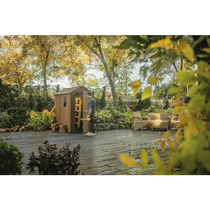 Keter Caseta de jardín Darwin 4x6 - Medidas ext. (An x Pr): 125,8 x 184,5 cm, Plástico, Marrón, 2,3 m² - Imagen de una caseta de herramientas de madera con las puertas abiertas en un patio mientras un hombre guarda una escalera amarilla y un cortasetos.