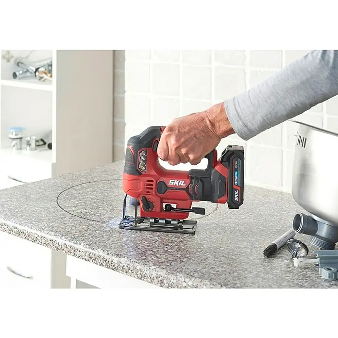 Skil PWRCore 20V Sierra de calar a batería con acción pendular 3420 CA - 20 V, Sin batería, Número de carreras marcha en vacío: 0 /min - 2.800 /min - La imagen muestra una sierra de calar SKIL roja cortando una forma circular en una encimera.