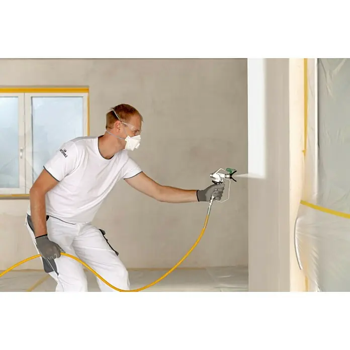 Wagner High Efficiency Airless Sistema de pulverización de pintura Power Painter 90 - 800 W, Caudal: 1,9 l/min - Un hombre está rociando pintura en una pared con un rociador de pintura, usando una máscara y gafas para protegerse.