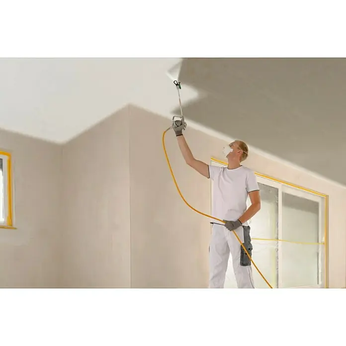 Wagner High Efficiency Airless Sistema de pulverización de pintura Power Painter 90 - 800 W, Caudal: 1,9 l/min - Un pintor rocía pintura sobre un techo con un pulverizador de pintura mientras que las ventanas y las puertas están cubiertas con cinta.