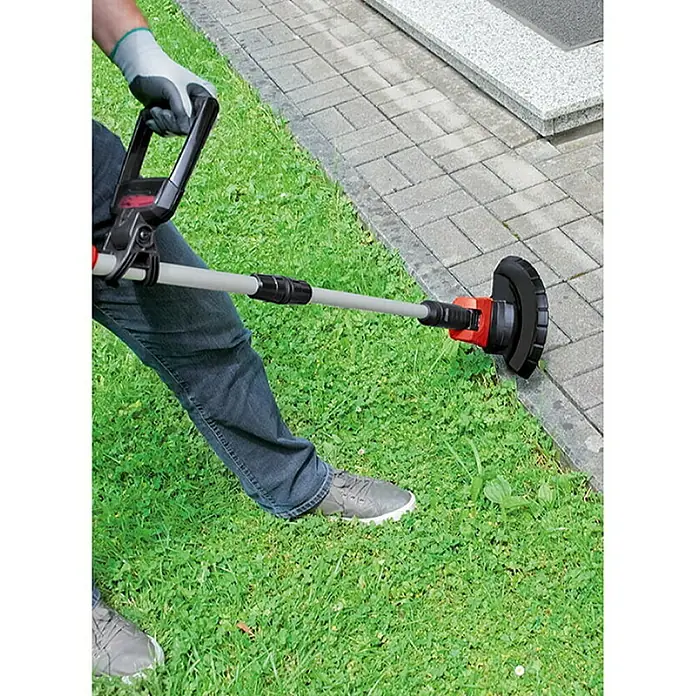 Einhell PXC 18V Recortabordes de batería GE-CT 18 Li-Solo - 18 V, Iones de litio, Sin batería - Un recortabordes en acción, cortando hierba en el borde de un camino. El dispositivo es negro y rojo, con un eje gris.