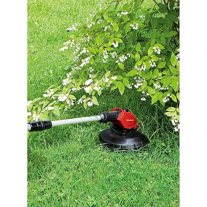 Einhell PXC 18V Recortabordes de batería GE-CT 18 Li-Solo - 18 V, Iones de litio, Sin batería - Cortabordes inalámbrico con carcasa roja y cabezal de corte negro debajo de un arbusto en flor.