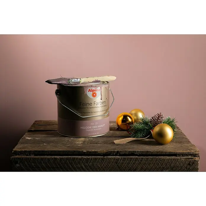 Alpina Wandfarbe Feine Farben - Melodie der Anmut, Matt, 2,5 l, Konservierungsmittelfrei - Alpina Feine Farben Lackdose mit Pinsel und Weihnachtskugeln auf einer Holzkiste vor einem rosa Hintergrund.