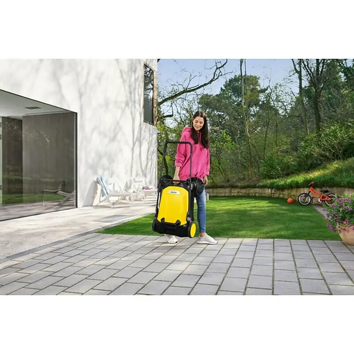 Kärcher Barredora manual S 4 Twin - Volumen de recipiente: 20 l, Rendimiento por unidad de superficie: 2.400 m²/h - Mujer con barredora Kärcher en el patio. La barredora es amarilla y negra.
