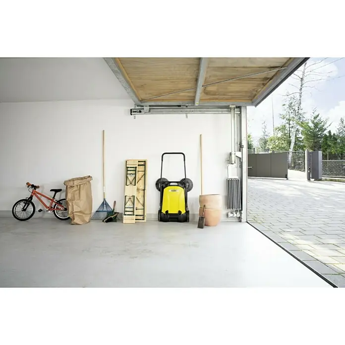 Kärcher Barredora manual S 4 Twin - Volumen de recipiente: 20 l, Rendimiento por unidad de superficie: 2.400 m²/h - Foto interior de un garaje con una barredora Kärcher, una bicicleta, un rastrillo y varios objetos domésticos.