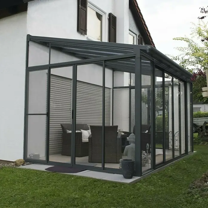 Palram – Canopia Porche acristalado San Remo - An x Pr x Al: 4,25 x 3 x 3,1 m, Gris antracita - Una moderna veranda de vidrio con marcos grises y muebles en el interior. La veranda ofrece un espacio luminoso y protegido en el jardín.