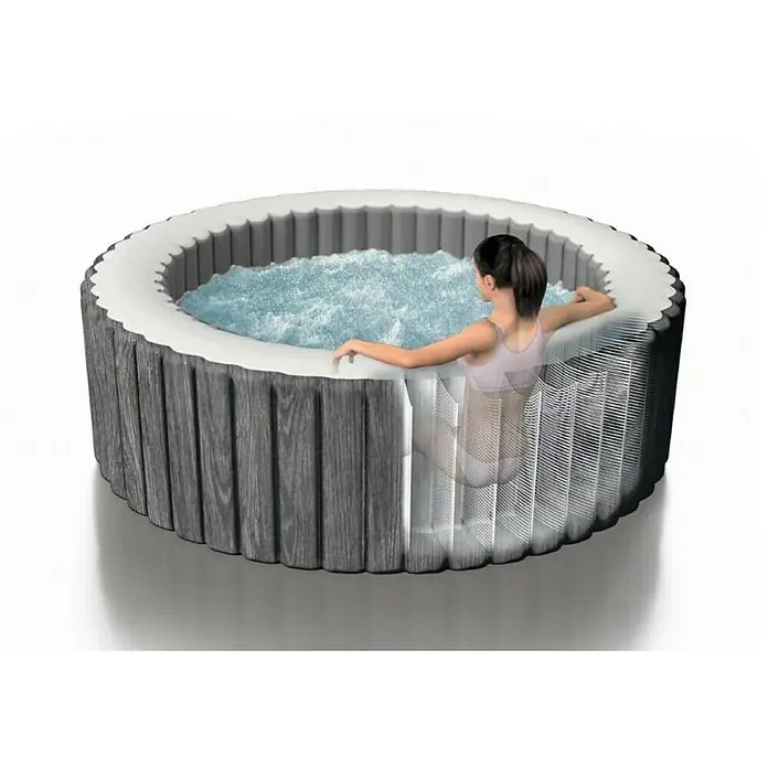 Intex Pure Spa Hidromasaje móvil Greywood Deluxe - Ø x Al: 196 x 71 cm, Gris/Blanco, 795 l - Imagen de una bañera de hidromasaje redonda con revestimiento de madera y una mujer relajándose dentro. Ideal para el jardín.