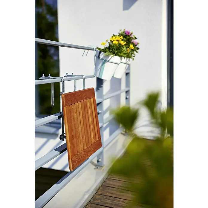 Sunfun Balkontisch - L x B x H: 40 x 60 x 1,5 cm, Akazie, Klappbar, Rechteckig, Natur - Holzfarbener Balkontisch hängt an einem grauen Geländer mit einem Topf gelb-lila Blumen.