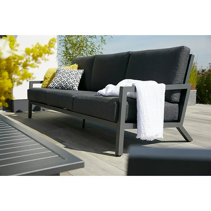 Sunfun Maja Conjunto de muebles - 4 pzs., Poliéster/Aluminio, Antracita - Un sofá moderno de jardín gris con cojines y una manta blanca en un patio.